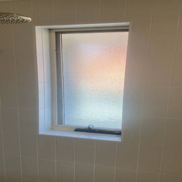 Window set into a white tiled wall, with tiled reveals around the frame
