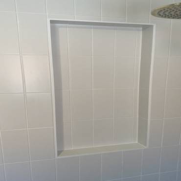 Large recessed shower niche lined with white wall tiles