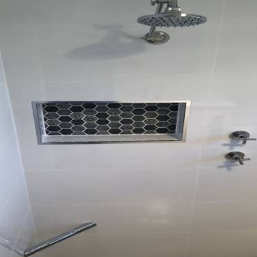 Shower wall with a recessed niche lined in dark hexagon mosaic
