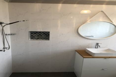 Shower wall with a dark mosaic niche beside a round mirror and timber-top vanity