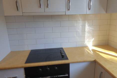 A kitchen with a white subway-tile splashback between a timber-look benchtop and white wall cabinets, with a black cooktop