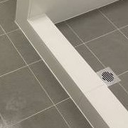 Close-up of the line where a white bath hob meets grey floor tiles, beside a floor waste