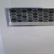 Close-up of a shower niche with dark hexagon mosaic tiles and a metal trim, set into white wall tiles